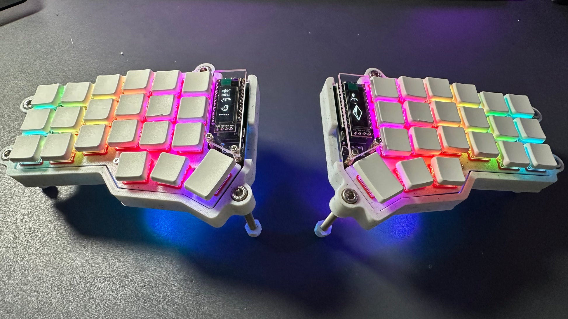 Corne Choc RGB low profile split keyboard at an angle, raised on tenting legs, dual OLED screens showing battery level — white case, white keycaps
