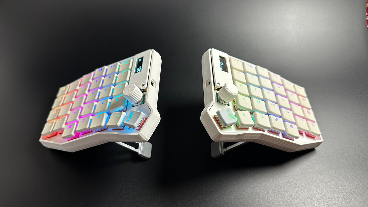 Sofle Choc split keyboard in white raised on its built-in retractable tenting legs, with translucent keycaps and dual OLED screens
